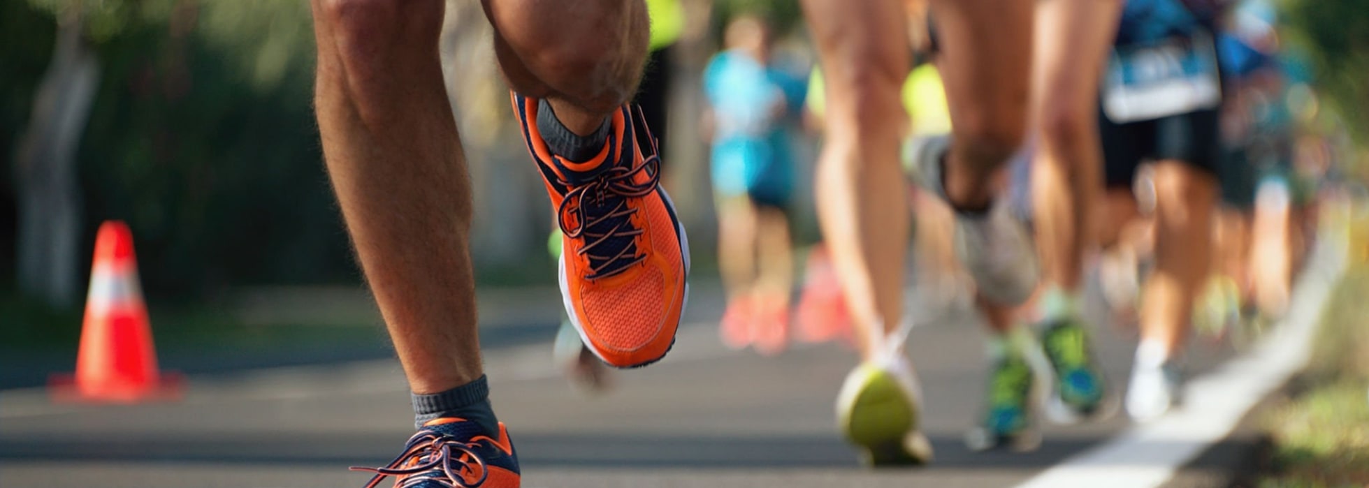 Close-up of runners' legs and shoes during a marathon on a sunny day, with orange sneakers in focus.